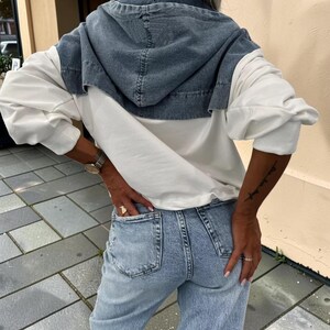 May include: A denim hooded jacket with white sleeves and light blue jeans. The jacket has a blue denim hood and a white body. The jeans are light blue and have pockets.