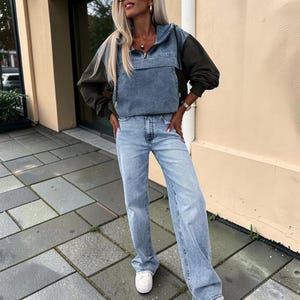 May include: A denim and olive green anorak-style jacket with a front zipper and a light blue denim panel. The jacket is paired with light blue, wide-leg jeans and white sneakers. The outfit is casual and stylish.