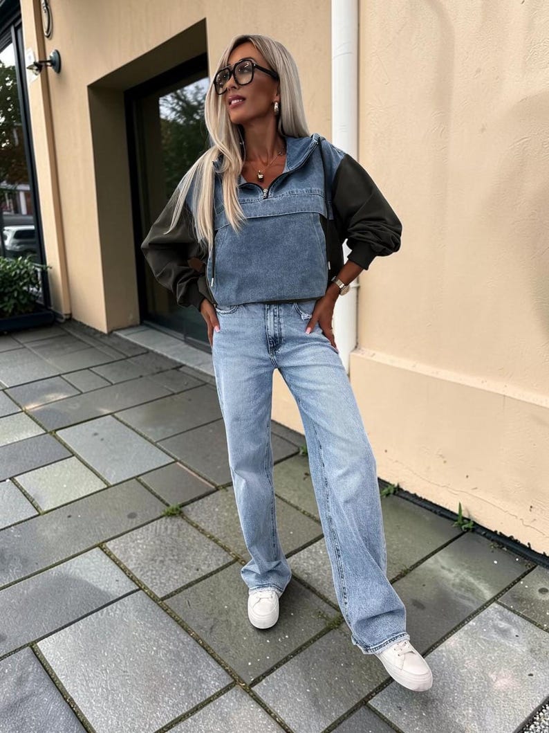 May include: A denim and olive green anorak-style jacket with a front zipper and a light blue denim panel. The jacket is paired with light blue, wide-leg jeans and white sneakers. The outfit is casual and stylish.