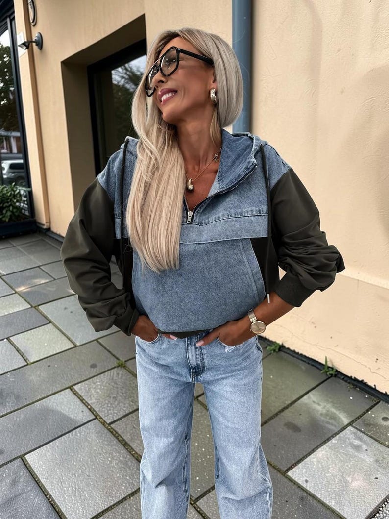 May include: A denim and olive green hooded jacket with a front zipper, paired with light blue jeans. The jacket has a color-block design, with denim on the upper body and olive green sleeves. The jeans are a light wash.