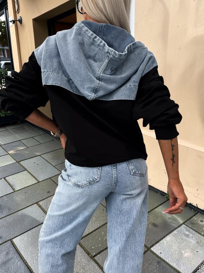 May include: Black hooded jacket with a light blue denim hood and shoulders. The jacket has long black sleeves and is paired with light blue denim jeans. The model is wearing black sunglasses.