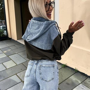 May include: A denim hooded jacket with olive green sleeves and light blue jeans. The jacket has a light blue denim hood and a drawstring. The jeans are light blue with a straight leg fit.