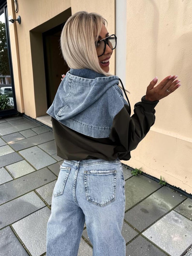 May include: A denim hooded jacket with olive green sleeves and light blue jeans. The jacket has a light blue denim hood and a drawstring. The jeans are light blue with a straight leg fit.