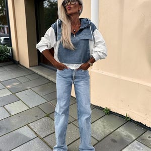 May include: A woman's outfit featuring a denim and white hooded jacket, light blue jeans, and white sneakers. The jacket has a denim front and white sleeves. The jeans are a light wash, and the sneakers are low-top.