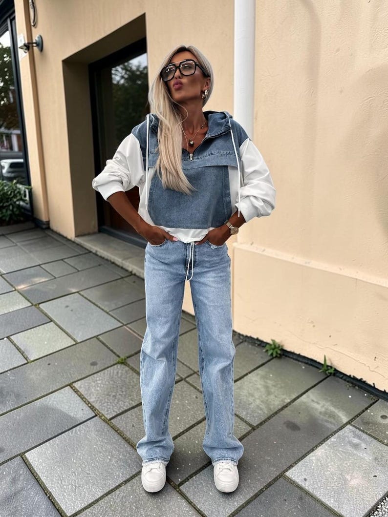May include: A woman's outfit featuring a denim and white hooded jacket, light blue jeans, and white sneakers. The jacket has a denim front and white sleeves. The jeans are a light wash, and the sneakers are low-top.