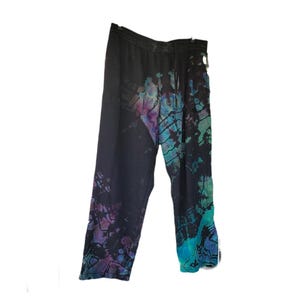 May include: Black tie-dye pants with a drawstring waist. The pants feature a vibrant pattern of teal, purple, and blue hues. The loose-fitting pants are made of a soft material.