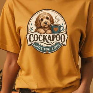 Könnte beinhalten: Ein senfgelbes Kurzarm-T-Shirt mit einer kreisförmigen Grafik, die einen braunen Cockapoo-Hund mit einer blauen Kaffeetasse mit Herz zeigt. Der Text COCKAPOO, COFFEE, DOGS, REPEAT steht in einer Vintage-Schriftart innerhalb des Emblems.