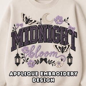 May include: A beige crewneck sweatshirt featuring an embroidered design with the text MIDNIGHT bloom. The graphic includes two butterflies, a crescent moon, purple flowers, two hanging lanterns, and small bows in a dark purple and cream color palette.