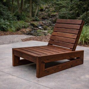 Puede incluir: Tumbona de exterior de madera marrón oscuro con asiento y respaldo de listones. La silla tiene una base rectangular y un respaldo inclinado. Está colocada sobre un patio de hormigón, ideal para relajarse al aire libre.