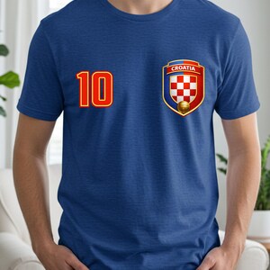 May include: A blue t-shirt featuring the number 10 in red with a gold outline on the left side. On the right side is a Croatian crest with a red and white checkered pattern, the word "Croatia", and a soccer ball.