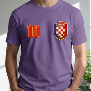May include: A purple t-shirt featuring the number 10 in red with a gold outline on the left chest. On the right chest is a Croatian national team crest with a red and white checkered pattern, a gold soccer ball, and the word "CROATIA".