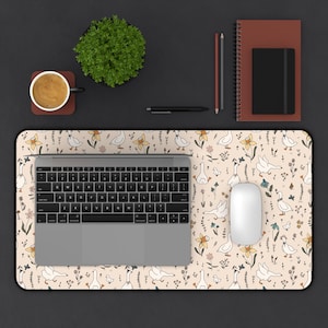 May include: A beige desk mat with a pattern of geese, flowers, and butterflies. A laptop, mouse, coffee cup, plant, and stationery are arranged on the mat. The mat is rectangular and designed for a workspace.