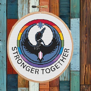 Op de afbeelding: Een ronde borduurring met een kruissteekontwerp van een zwart silhouet van een duiker in een regenboogkleurige ring. De tekst STRONGER TOGETHER is in zwarte hoofdletters langs de onderkant van het ronde frame geborduurd.