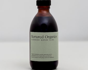 May include: A dark amber glass bottle with a black screw cap containing a dark liquid. The label is light green with black text reading Nurtured Organics, ELDERBERRY NURTURE BLEND, and a description of the organic elderberry syrup contents.