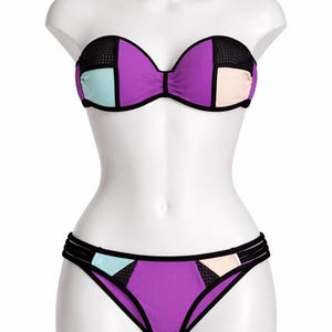 May include: A two-piece bikini set on a mannequin. The top is a strapless design with a purple base, black mesh accents, and colour block details in light blue and peach. The bottoms are purple with matching colour block details.