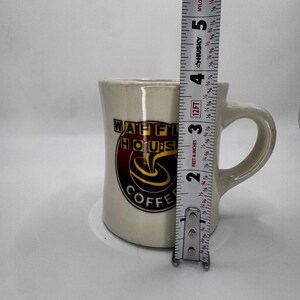 May include: Cream-colored ceramic coffee mug with the "WAFFLE HOUSE COFFEE" logo in red, yellow, and black. The mug is approximately 3.5 inches tall. It has a curved handle and a slightly flared rim.