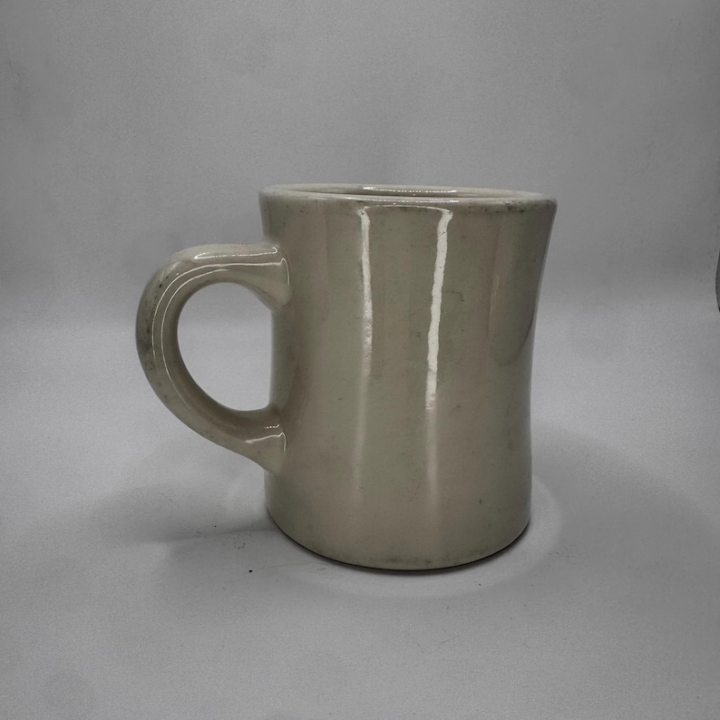 May include: A cream-colored ceramic mug with a rounded handle. The mug has a simple, classic design, suitable for coffee or tea. The mug is made of a sturdy material and is likely dishwasher safe.