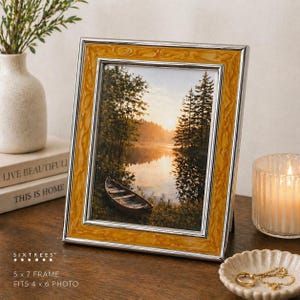 May include: A 5x7 inch photo frame with a landscape image. The frame has a silver border and a textured, amber-colored inner frame. The image shows a lake scene with a boat, trees, and a sunrise. The text "SIXTREES" is visible.