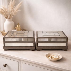 Puede incluir: Dos joyeros decorativos de madera con tapas espejadas y diseños geométricos. Las cajas tienen un marco marrón oscuro y una base de color claro. Un pequeño plato con joyas está cerca.