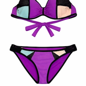 May include: A two-piece swimsuit in a vibrant colour block design. The bikini top features a bow tie closure and the bottoms have a classic cut. The colour scheme includes purple, black, light blue, and beige.