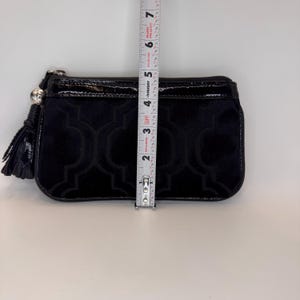 May include: Black velvet clutch with a geometric pattern and patent leather trim. The clutch is approximately 13 cm long, with a tassel and silver-tone hardware.