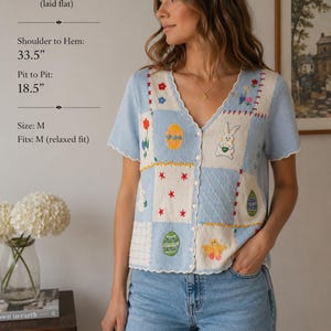 May include: A light blue and cream-colored cardigan with a patchwork design featuring embroidered Easter-themed motifs. The cardigan has a V-neck, short sleeves, and a button-up front. Shoulder to hem: 33.5 inches. Pit to pit: 18.5 inches. Size M.
