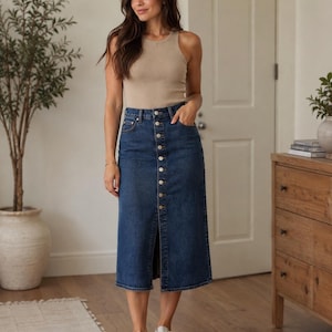 May include: A beige ribbed sleeveless tank top paired with a dark blue denim midi skirt featuring a front button-down closure, a high waist, and a straight hemline. The skirt includes classic five-pocket styling and a central vertical seam.
