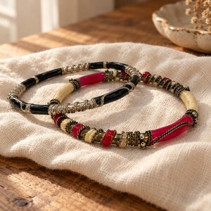 May include: Two circular bangles featuring alternating segments of glossy black, cream, and vibrant pink resin. The segments are separated by intricate, textured metallic wire wrappings and small silver-toned metal beads.