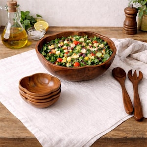 Puede incluir: Un letrero de madera rústico blanco con la palabra "Welcome" escrita a mano. El letrero tiene un aspecto envejecido y un elemento floral decorativo. El fondo es una textura de madera borrosa.