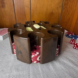 May include: A dark brown, circular, molded plastic poker chip carousel with multiple vertical slots. The carousel is filled with stacks of red and white poker chips. Two small, cream-colored rectangular inserts are visible on the top surface.