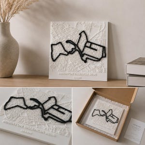 May include: A square white wall art piece featuring a raised 3D map of Valencia with a prominent black thread outline of a marathon route. The text MARATON VALENCIA 2026 and 42.2 KM is embossed at the bottom. The piece is shown displayed and in a box.