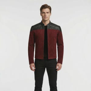 May include: A burgundy suede jacket with black leather shoulder detailing. The jacket features a classic collar and a front zip. The model is wearing black trousers.