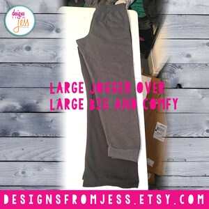 May include: Two pairs of sweatpants, one grey and one black, folded on a white surface. The grey sweatpants have a cuffed hem. The text "LARGE JOGGER OVER LARGE BIG AND COMFY" is printed in pink on the white surface.