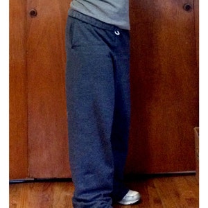 May include: A pair of dark grey sweatpants with a drawstring waist. The sweatpants are shown on a person standing in front of a wooden door. The text "Size Small in Black Heather" is visible at the bottom of the image.