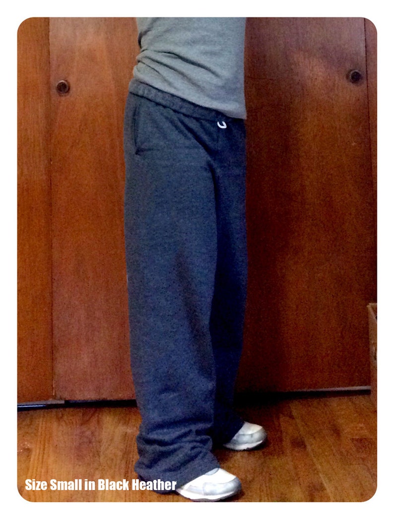 May include: A pair of dark grey sweatpants with a drawstring waist. The sweatpants are shown on a person standing in front of a wooden door. The text "Size Small in Black Heather" is visible at the bottom of the image.