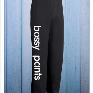 May include: Black sweatpants with the words "bossy pants" printed vertically in white on the left leg.