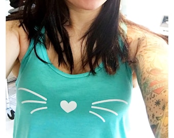 May include: A turquoise tank top with a white cat face design. The cat face has a heart for a nose and whiskers.