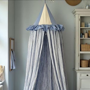 Könnte beinhalten: Ein blau-weiß kariertes Himmelbett mit Rüschenbesatz. Das Baldachin hat eine konisch geformte Oberseite mit einem hellbeigen Mittelteil. Die Vorhänge sind geöffnet und geben den Blick ins Innere frei.