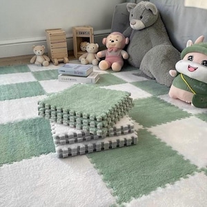Puede incluir: Losetas de suelo de espuma entrelazadas en tonos verdes y blancos, creando un patrón de cuadros. Las losetas son suaves y afelpadas. La escena incluye peluches y objetos decorativos, sugiriendo un área de juegos para niños.