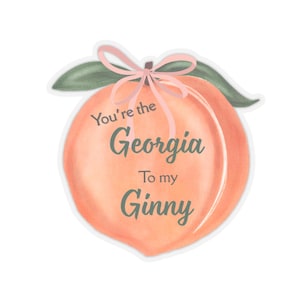 Può includere: Un adesivo a forma di pesca con la scritta "You're the Georgia To my Ginny". La pesca è in stile acquerello con sfumature di arancione e rosa, con foglie verdi e un fiocco rosa.