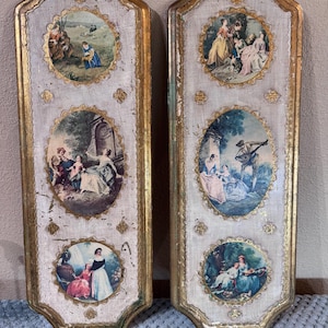 May include: Two tall, rectangular wall plaques with distressed white and gold frames. Each plaque features three oval-shaped, colorful pastoral scenes depicting figures in period clothing within ornate gold borders, set against a textured background.