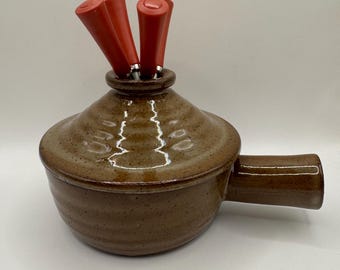 Donabe o pentola per fonduta in gres vintage con superficie screziata e quattro utensili rossi.