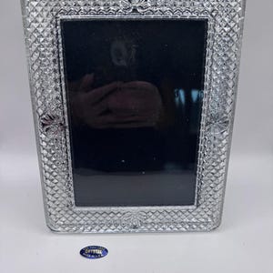 May include: A rectangular clear crystal picture frame featuring a diamond-cut textured border with embossed shell motifs at the top, bottom, and sides. A small blue oval sticker at the bottom reads 24% FULL LEAD CRYSTAL MADE IN U.S.A.
