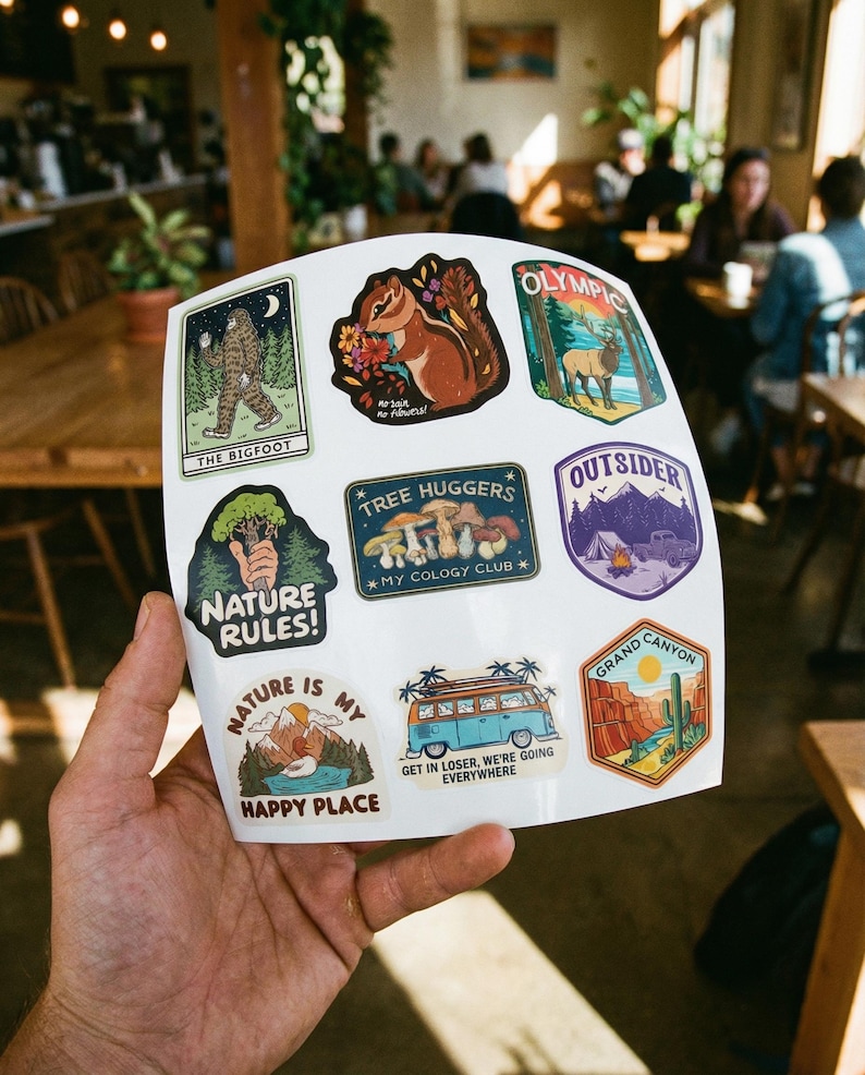 May include: A sheet of colorful stickers featuring nature-themed designs. The stickers include images of Bigfoot, a squirrel, mountains, a camper van, and the text "Nature Rules!" and "Grand Canyon".