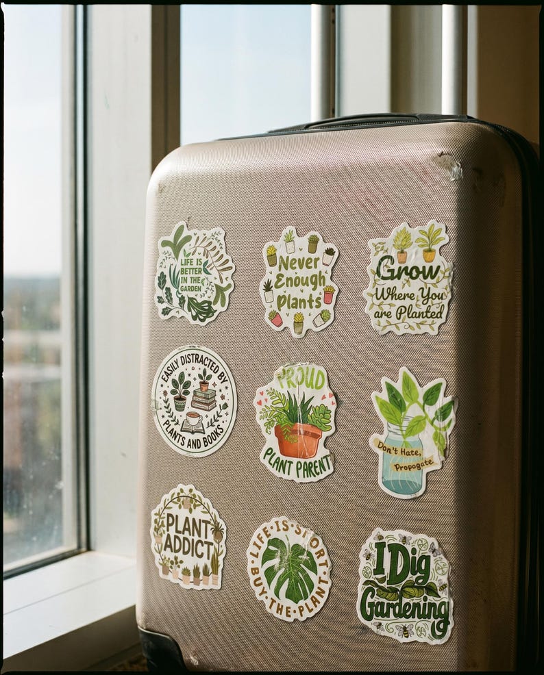 May include: A beige hard-shell suitcase decorated with nine plant-themed stickers featuring various green foliage illustrations and text including Life is Better in the Garden, Never Enough Plants, Grow Where You are Planted, and I Dig Gardening.