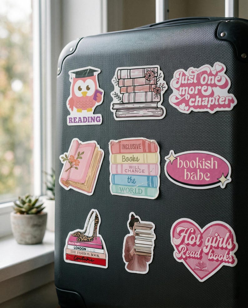 May include: A collection of colorful stickers on a black suitcase. The stickers feature book-related designs, including stacks of books, an owl with a graduation cap, and phrases like "Just One More Chapter" and "Hot girls Read books".
