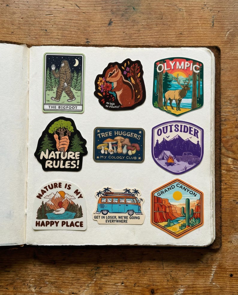 May include: A collection of colorful stickers with nature-themed designs. The stickers feature images of Bigfoot, a chipmunk, a deer, mountains, a camper, a Grand Canyon scene, and text that reads "Nature Rules!" and "Nature is my happy place."