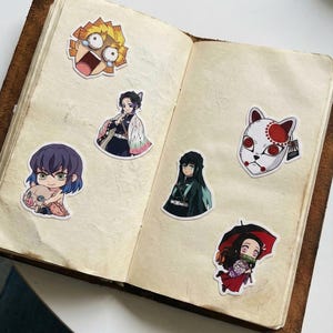 May include: A selection of anime character stickers, featuring a character with yellow hair and a surprised expression, a character with a fox mask, and more. The stickers are arranged on the open pages of a vintage-style journal.