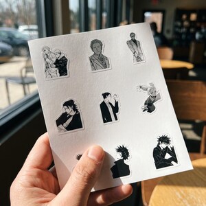 May include: A white sheet featuring eight individual black and white anime-style stickers. The designs depict various characters in different poses, including portraits, figures in suits, and dynamic stances, all rendered with detailed line work and shading.