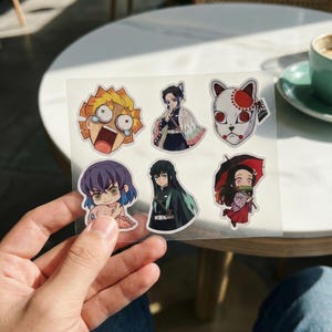 May include: A sheet of anime-style stickers featuring various characters. The stickers showcase vibrant colours and detailed illustrations of characters with distinct facial expressions and attire. The stickers are on a clear backing.